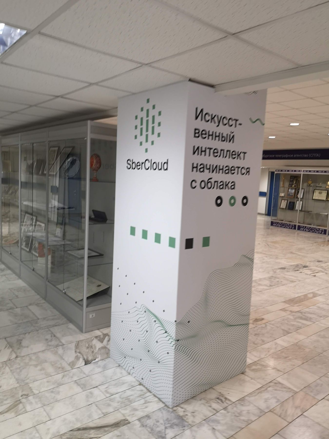 Колонна с логотипом SberCloud и слоганом «Искусственный интеллект начинается с облака» рядом с витринами музея ТАСС